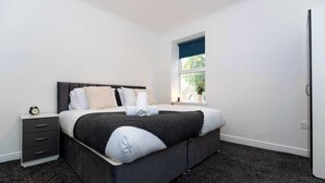 Een moderne slaapkamer met een groot bed, een nachtkastje, een raam met uitzicht en een deur.