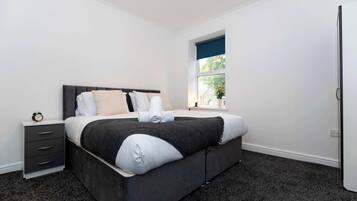 A modern bedroom with a large bed, a nightstand, a window with a view, and a door.