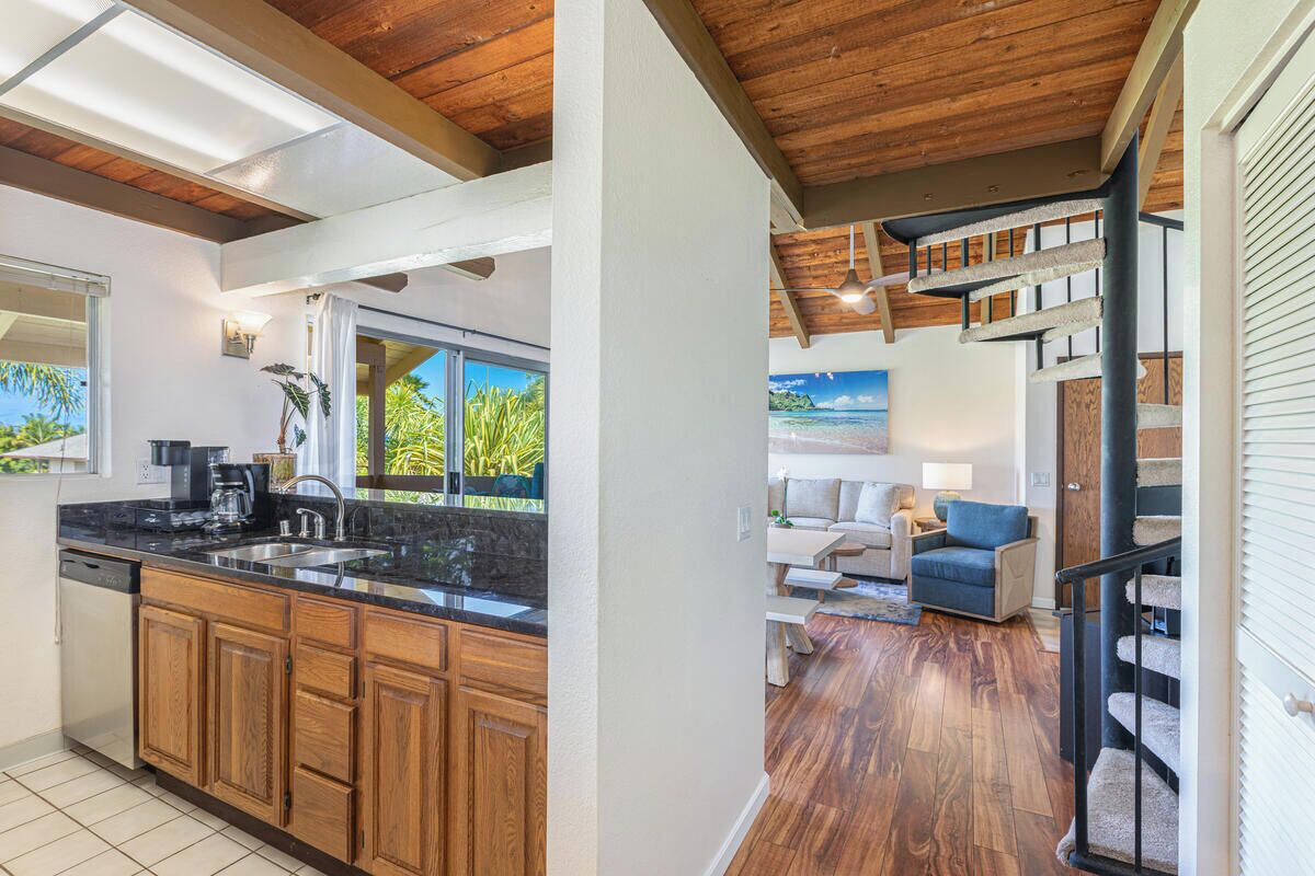A modern kitchen with wooden cabinets and a black countertop, a dining area with a view of the ocean, and a staircase with a cat tree.