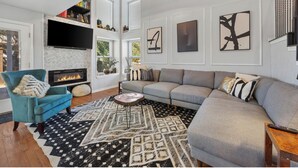Una sala de estar moderna con chimenea, un sofá grande, un sillón color turquesa y obras de arte en las paredes.
