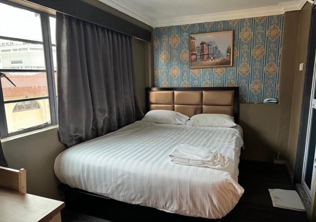 Quarto de hotel com cama, janela com cortinas, um quadro na parede e uma mesinha.