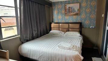 Quarto de hotel com cama, janela com cortinas, um quadro na parede e uma mesinha.