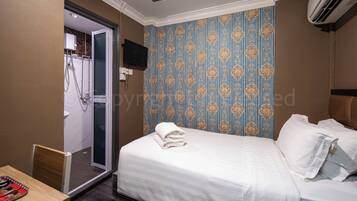 Habitación de hotel con cama, zona de ducha y televisor montado en la pared.