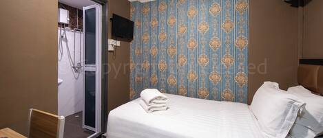 A hotel room with a bed, a shower area, and a television mounted on the wall.