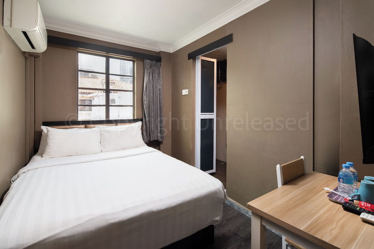 Une chambre d’hôtel avec un lit, une fenêtre, une table avec des bouteilles d’eau et une chaise.