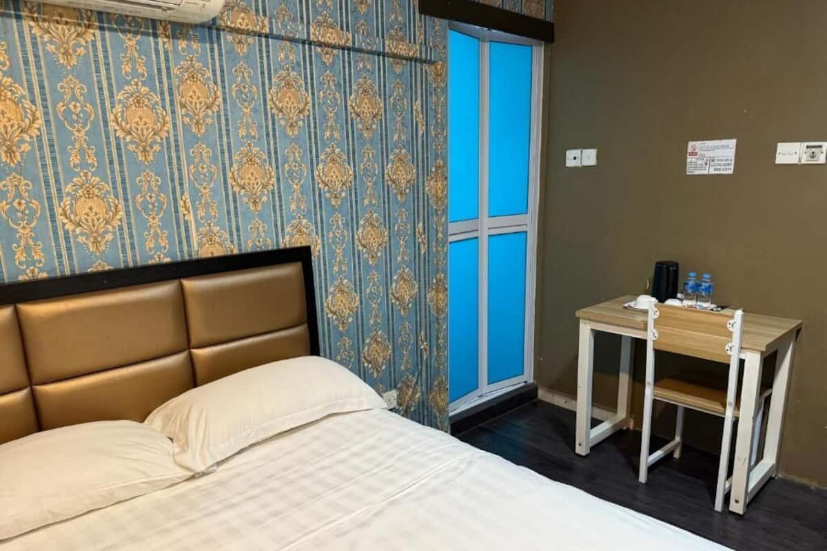 Une chambre d’hôtel avec un lit, une petite table, une fenêtre à cadre bleu et un papier peint à motifs.