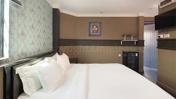 Quarto de hotel com cama grande, televisão de tela plana na parede e pequena mesa de trabalho com cadeira.