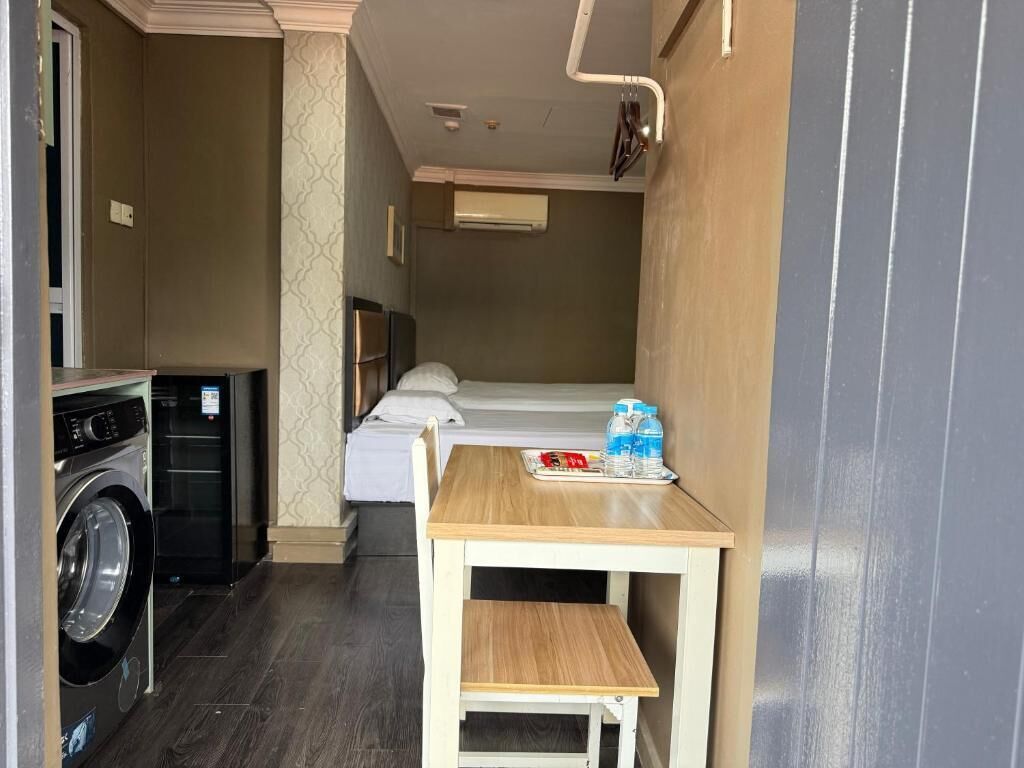 Ein kleines Hotelzimmer mit Waschmaschine, einem Tisch mit einer Tablett voller Gegenstände und einem Bett mit weißem Kopfteil.