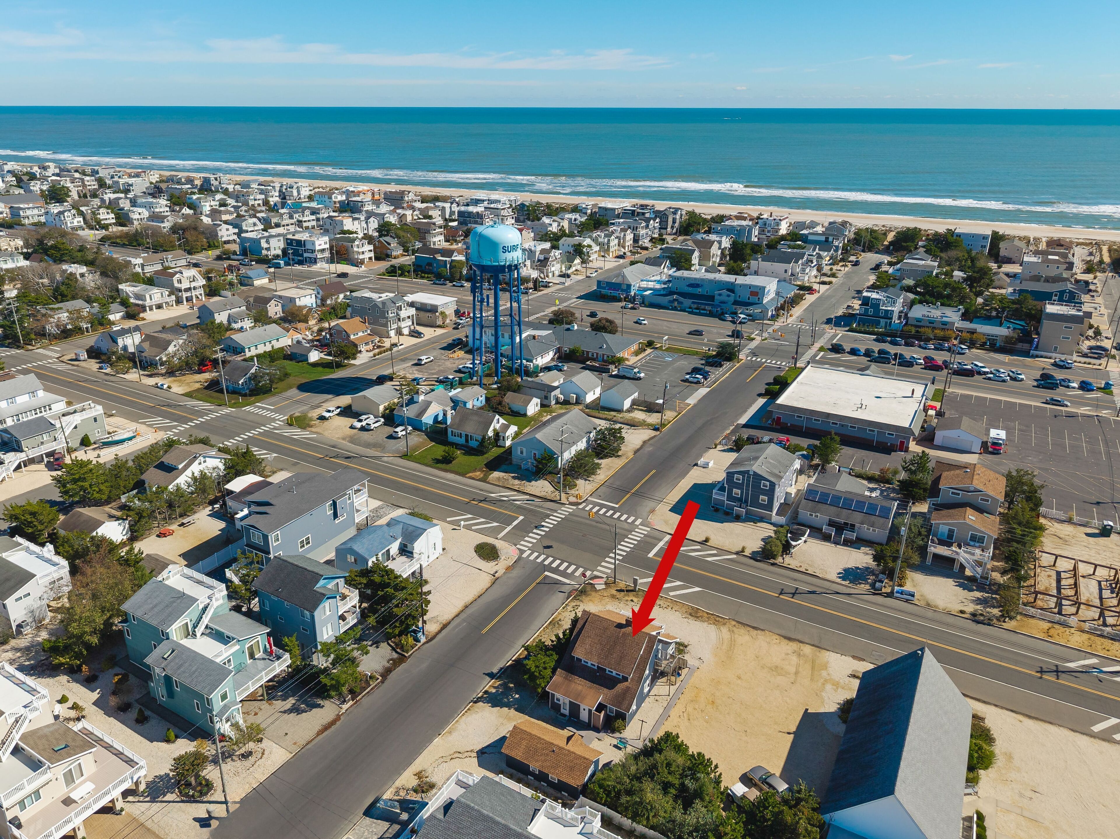 An aerial view of a coastal town with a prominent blue water tower, a main road, and a beach in the background.