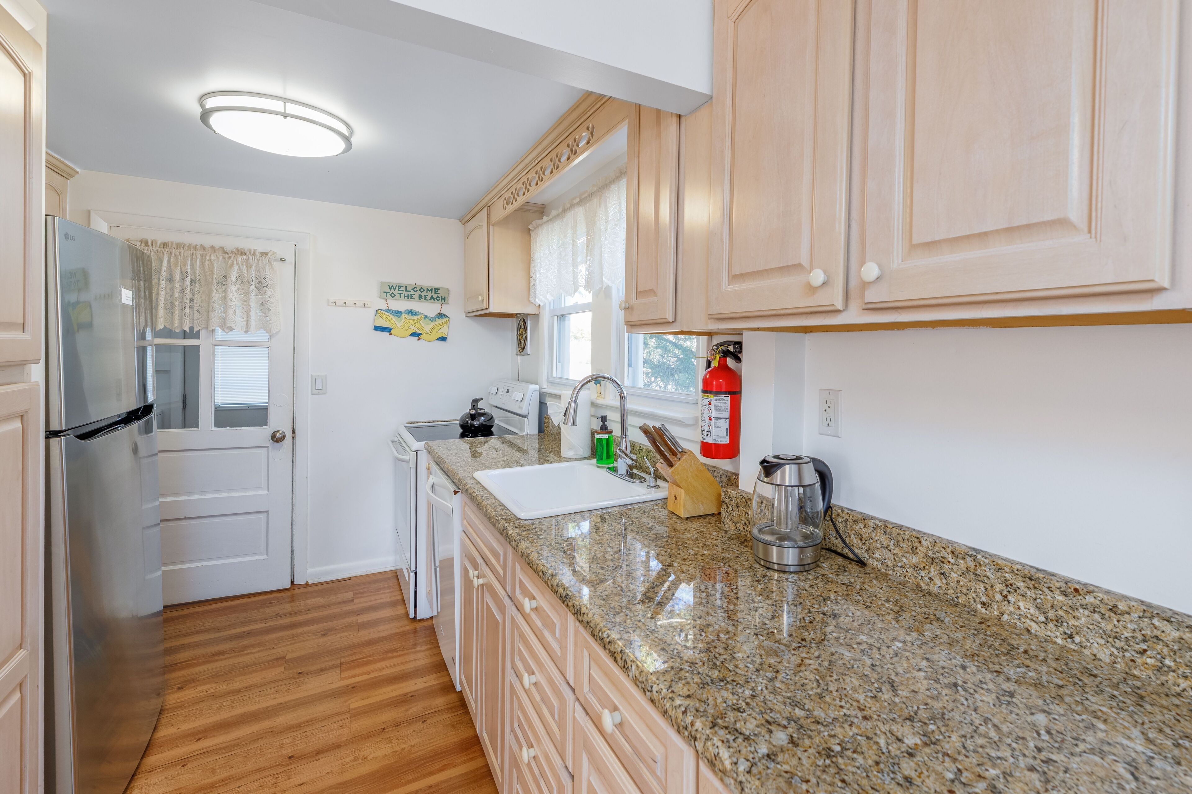 A kitchen with wooden cabinets, a granite countertop, a stainless steel sink, and a fire extinguisher.