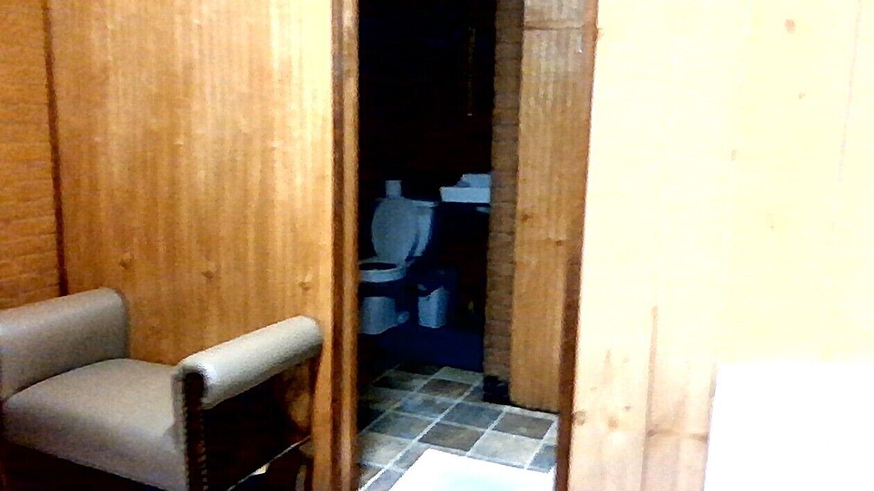 A wooden-framed bathroom with a toilet and a chair.