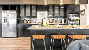 A modern kitchen with dark cabinets, stainless steel appliances, and a central island with bar stools.