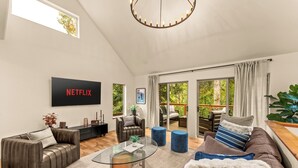 A modern living room with a glass coffee table, leather sofa, and a large TV screen displaying 'NETFLIX'. - Creek Front with Firepit Patio, BBQ & Theatre Near Hot Springs, Hiking, Biking (Glenwood Springs)