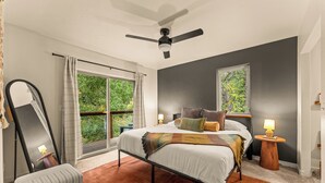 A bedroom with a bed, a large mirror, a bedside table with a lamp, and a view of greenery through a window. - Creek Front with Firepit Patio, BBQ & Theatre Near Hot Springs, Hiking, Biking (Glenwood Springs)