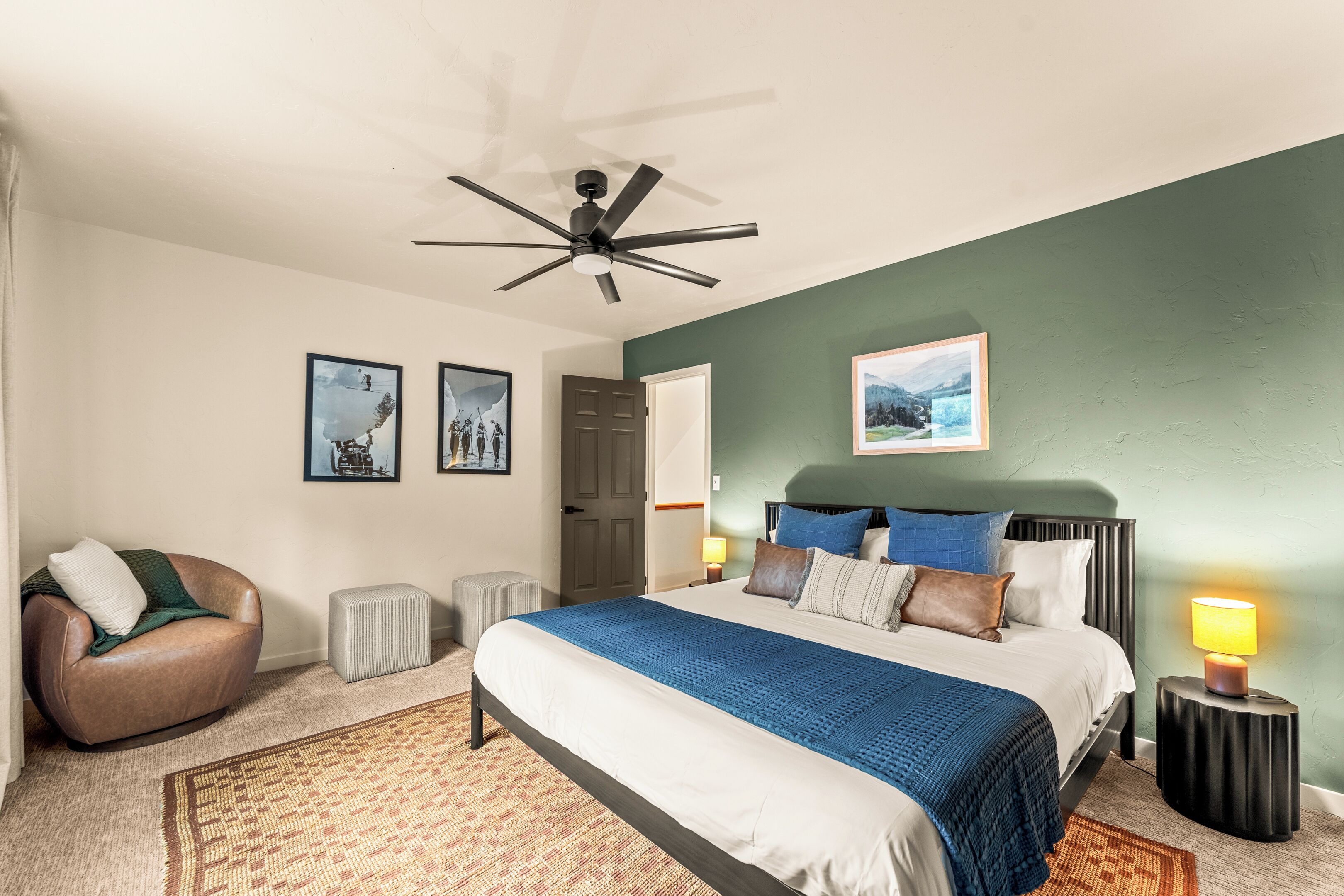 Une chambre à coucher avec un lit, une chaise, un ventilateur de plafond et une table de chevet avec une lampe.