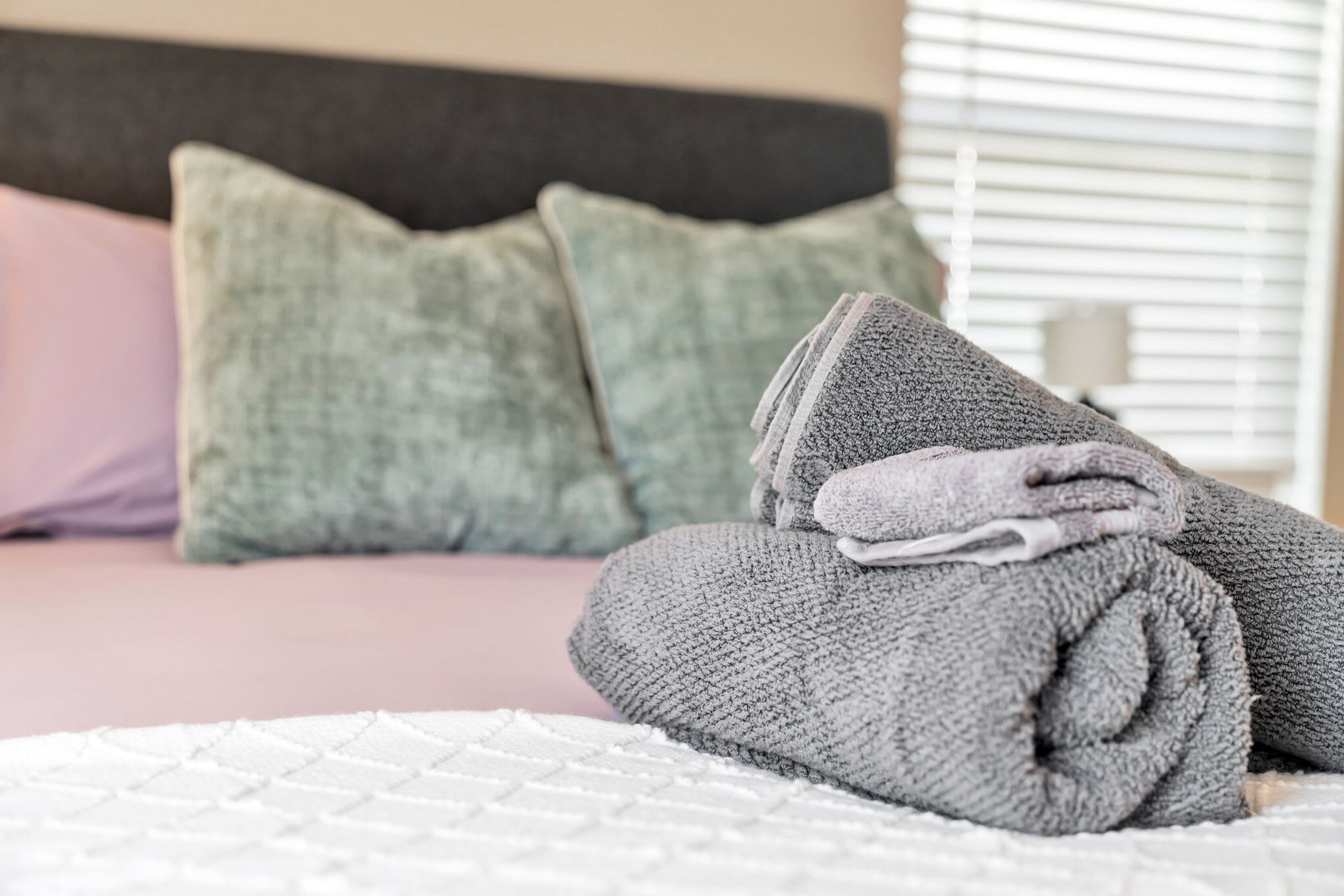 A neatly made bed with a folded gray towel and a pillow.