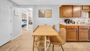 A dining area with a wooden table and chairs, a kitchen with wooden cabinets, and a hallway leading to a bedroom. - Close to beaches, BBQ, workout gear, private yard (Largo)