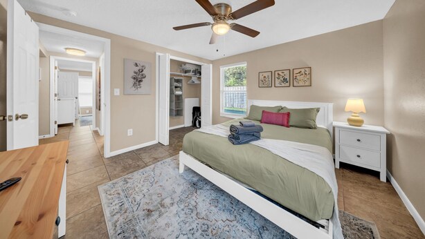 A bedroom with a bed, bedside table, nightstand, ceiling fan, and a view of the outside. - Close to beaches, BBQ, workout gear, private yard (Largo)