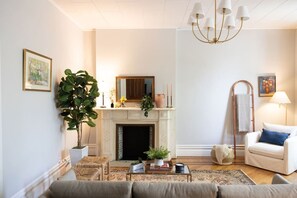 A living room with a fireplace, a sofa, a coffee table, and a chandelier. - Charming Apt. with Marble Mantel (Troy)