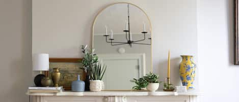 Une cheminée blanche ornée d’une console sur laquelle est posé un miroir, un lustre et divers objets décoratifs, notamment un vase, une bougie et un livre.