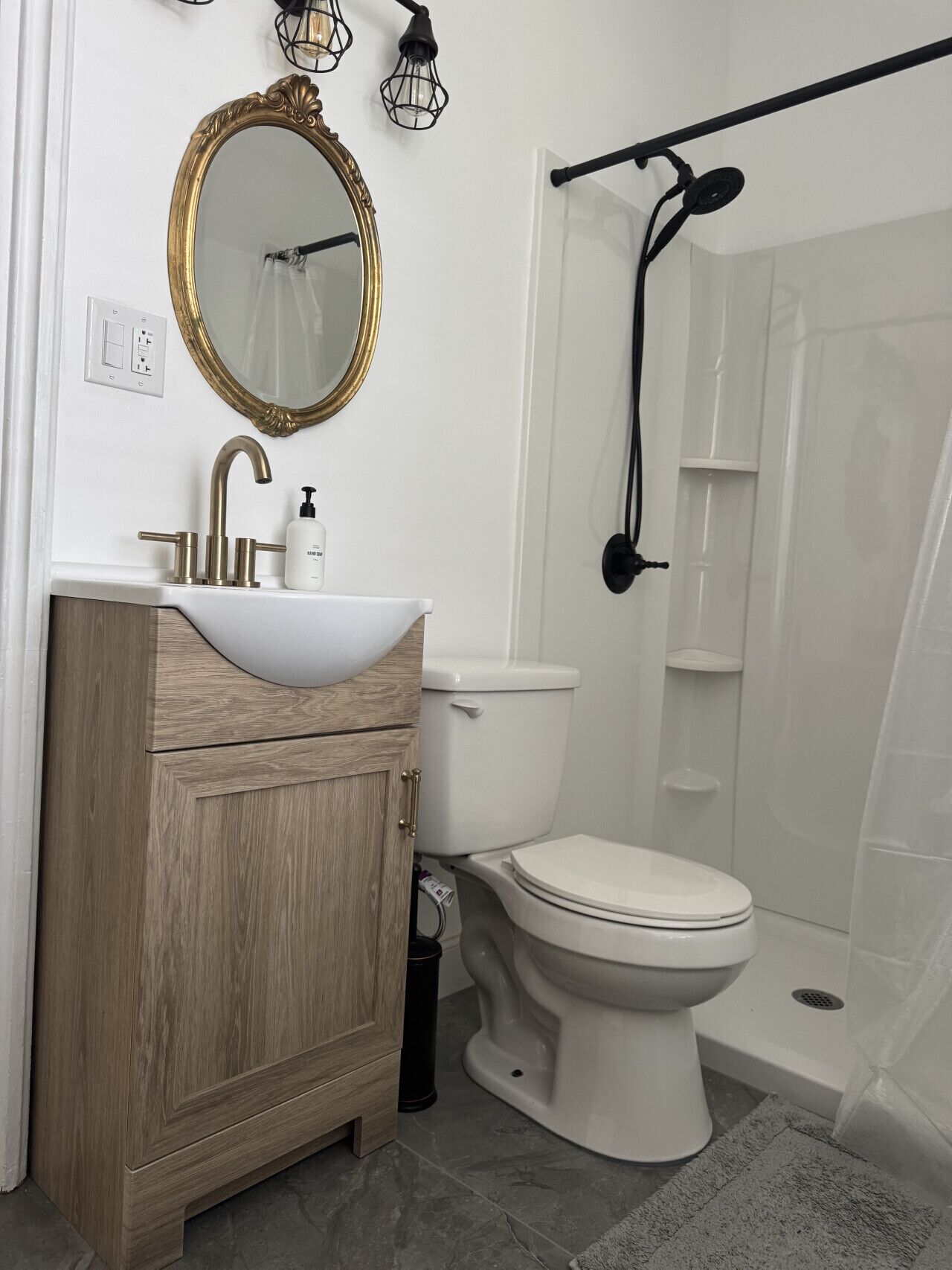 Un baño con tocador de madera, espejo con marco dorado, lavabo blanco, inodoro y zona de ducha.
