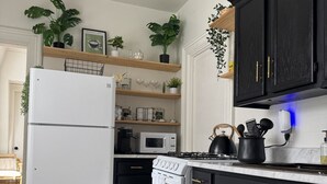 A kitchen with dark cabinets, a white refrigerator, a microwave, a stove, and a sink. There are plants on the shelves and a rug on the floor.