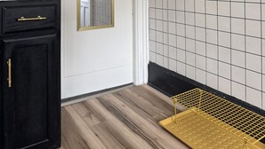 A kitchen with dark cabinetry, a white door, a mirror, a tiled backsplash, and a yellow cleaning mat.