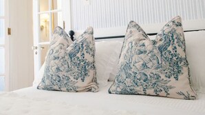 Ein Schlafzimmer mit einem Bett, zwei Zierkissen, einem Nachttisch und einer Tür zu einem anderen Raum.