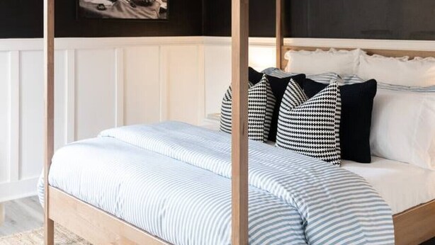 A four-poster bed with a striped bedspread and black and white pillows, set against a dark wall with a framed picture above it. - Peaceful, Artsy North Troy Riverview Apt (Troy)