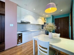 A modern kitchen with white cabinets, a dining table with chairs, and a pendant light. - Dalat Center Residence (Dalat)
