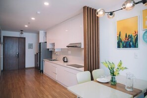 A modern kitchen with white cabinets, a stainless steel refrigerator, and a wooden door. - Dalat Center Residence (Dalat)