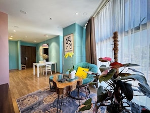 A modern living room with a glass coffee table, teal armchair, and a large window with sheer curtains. - Dalat Center Residence (Dalat)