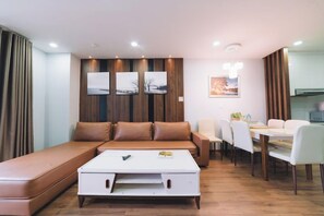 A modern living room with a sofa, a coffee table, and a dining area with chairs and a table. - Dalat Center Residence (Dalat)