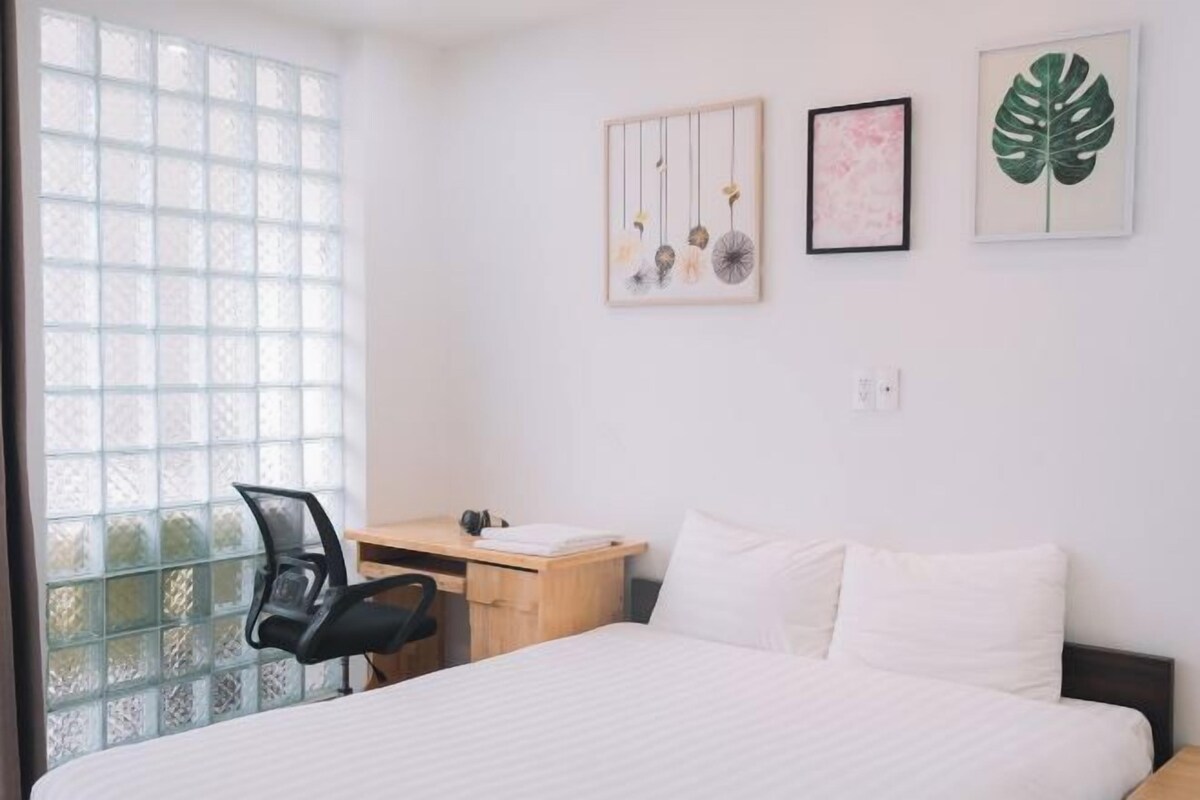 A hotel room with a bed, a desk, and a chair. There are three framed pictures on the wall.