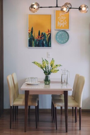 A dining area with a table set for two, a vase with yellow flowers, and wall art including a clock and a motivational quote. - Dalat Center Residence (Dalat)