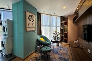 Una sala de estar moderna con una pared de acento color turquesa, un sillón verde, una mesita, un televisor de pantalla plana y un ventanal grande.
