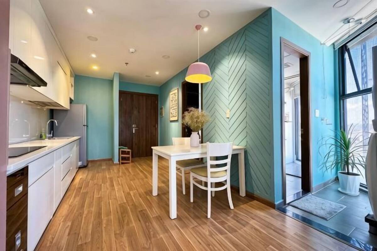 A modern kitchen with wooden flooring, a dining area with a white table and chairs, and a teal accent wall.