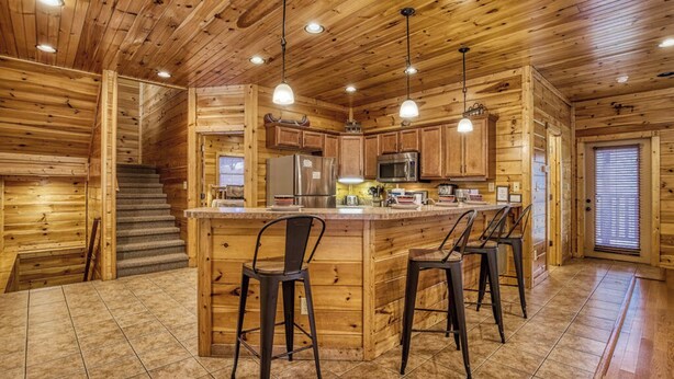 L’intérieur d’une cabane en bois comprend un espace cuisine avec un îlot central, des tabourets de bar et un escalier.