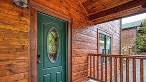 Une cabane en bois avec une porte verte, un porche en bois et un petit espace extérieur aménagé pour s’asseoir.