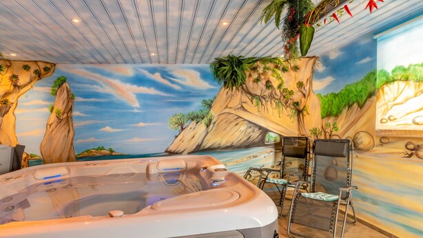 Een jacuzzi met een tropische muurschildering, een plafond met strepen en een zithoek met stoelen.