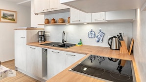 Een moderne keuken met witte kasten, een houten aanrecht, een inbouwvaatwasser en een fornuis.