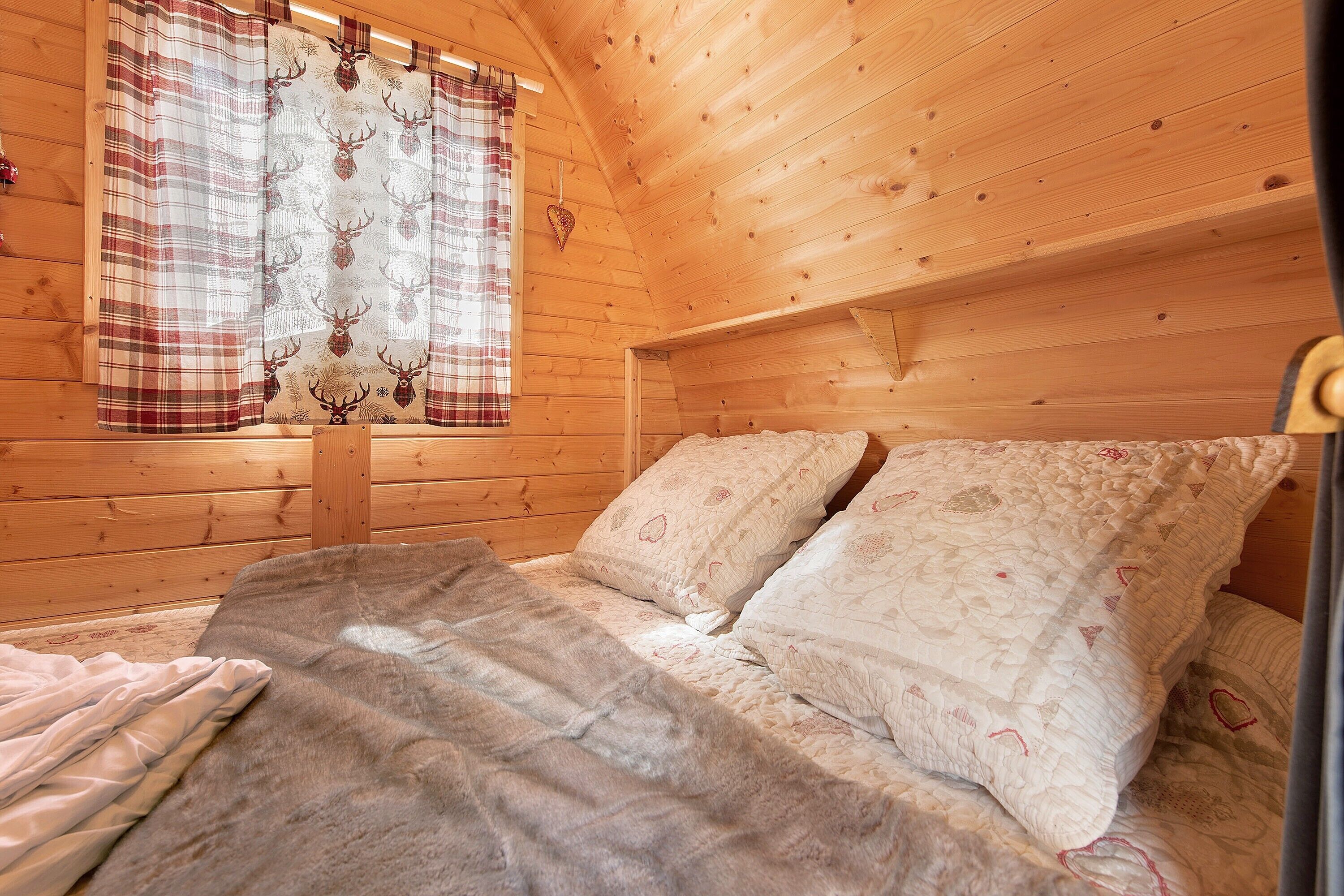 Un dormitorio acogedor tipo cabaña, con cama, almohadas y ventana con cortinas.