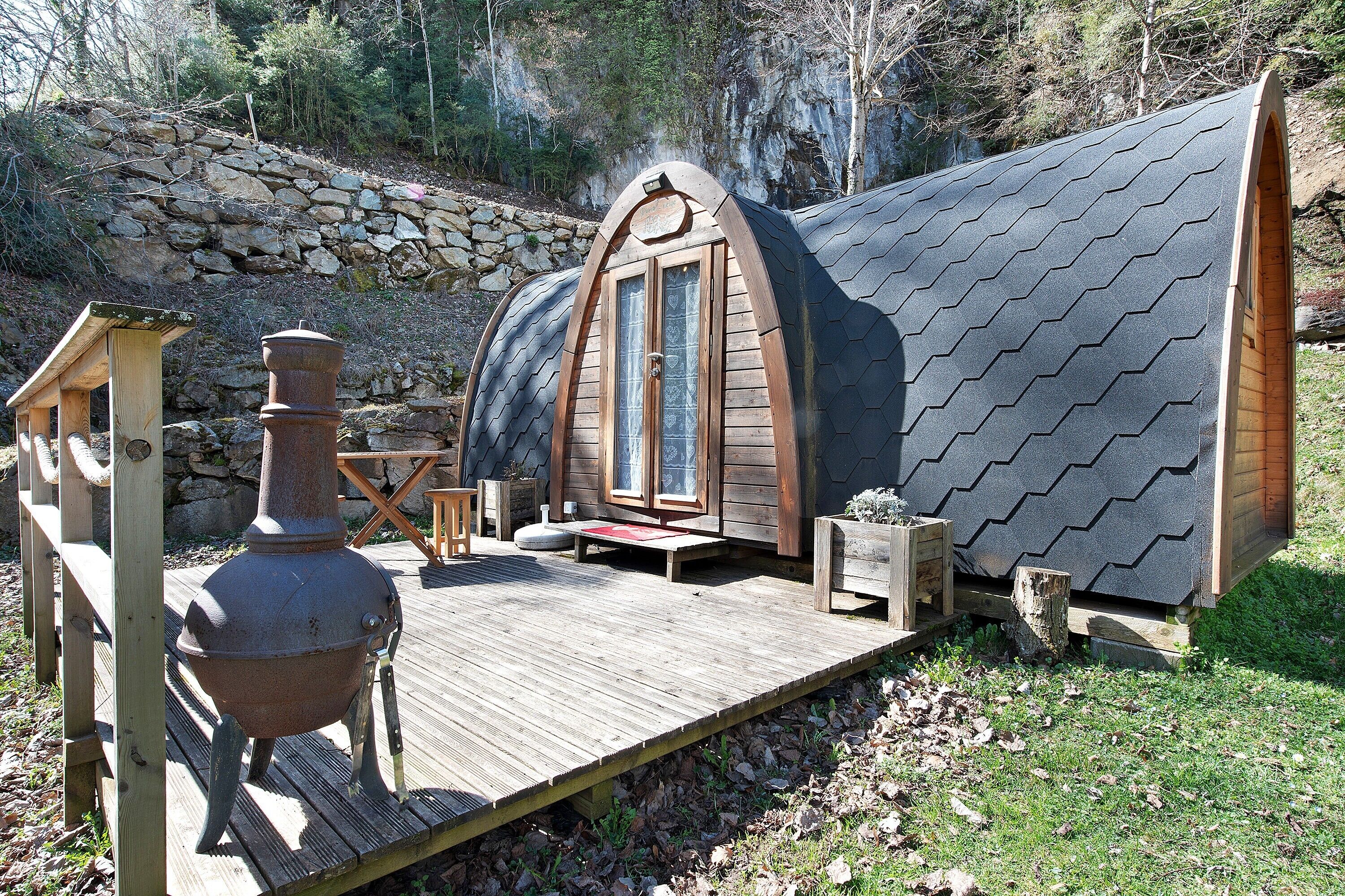 A wooden cabin with a sloped roof, a stone wall, and a wooden deck.