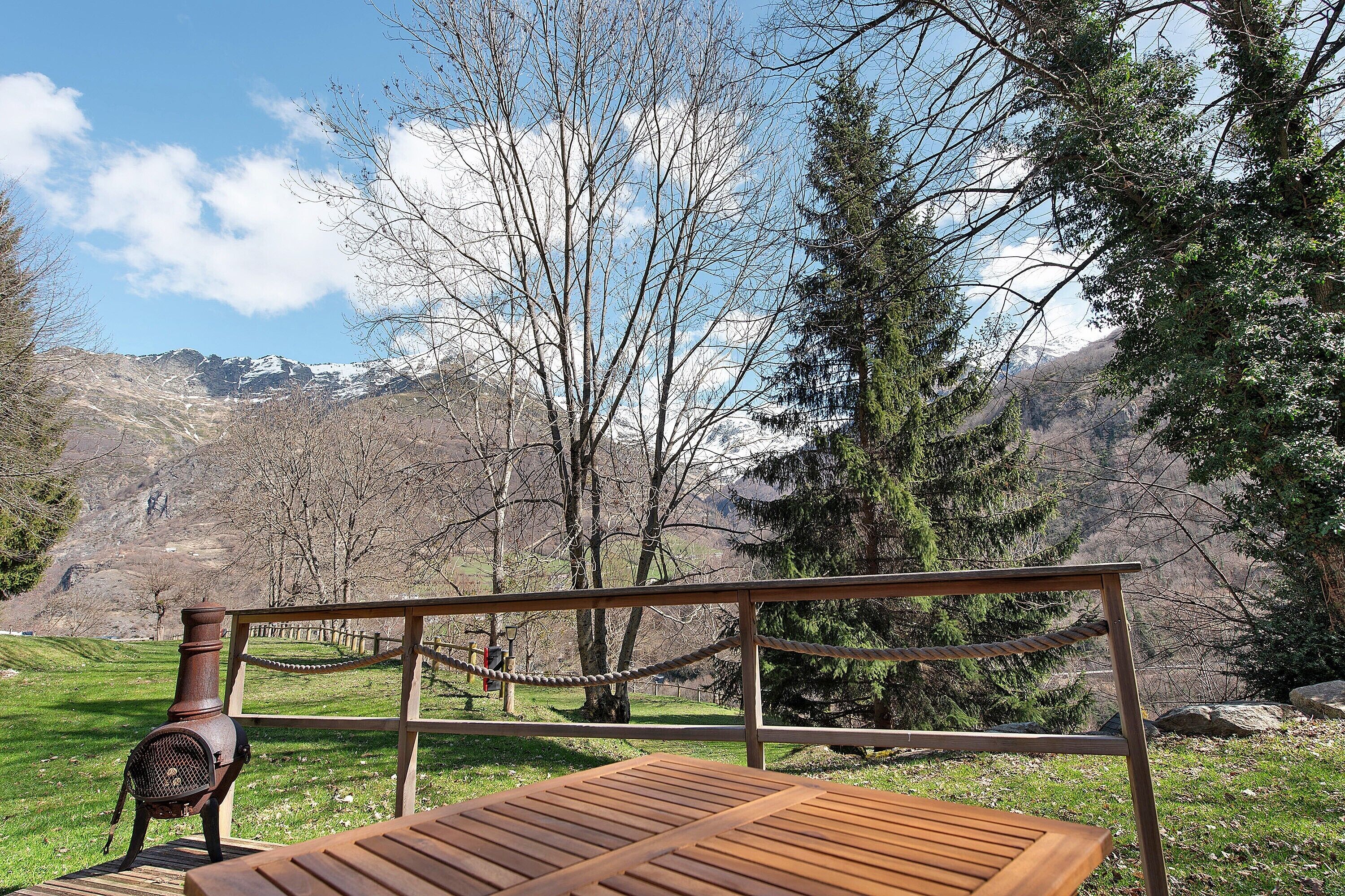 A wooden table and a rustic stove in a scenic outdoor setting with mountains in the background.