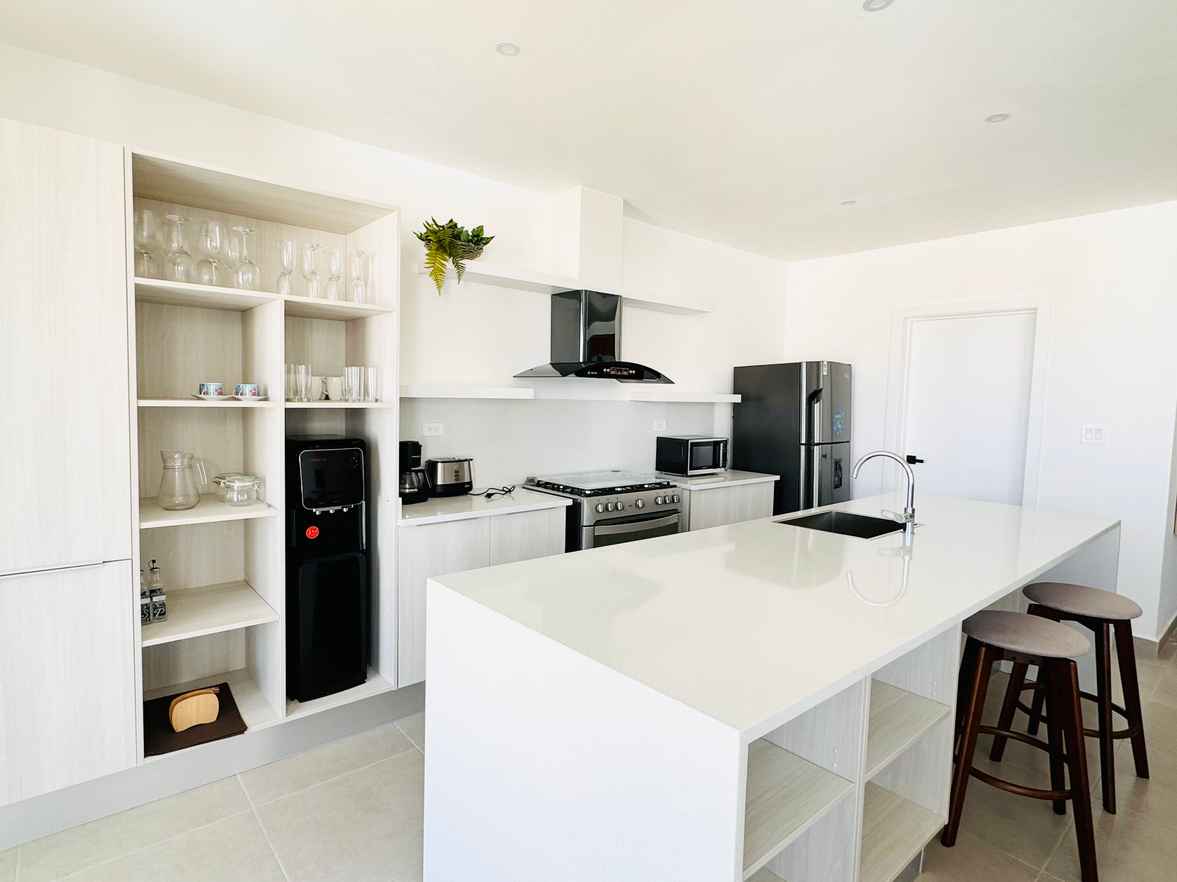 Une cuisine moderne avec des meubles blancs, un îlot central, des appareils en acier inoxydable et un four à micro-ondes encastré.