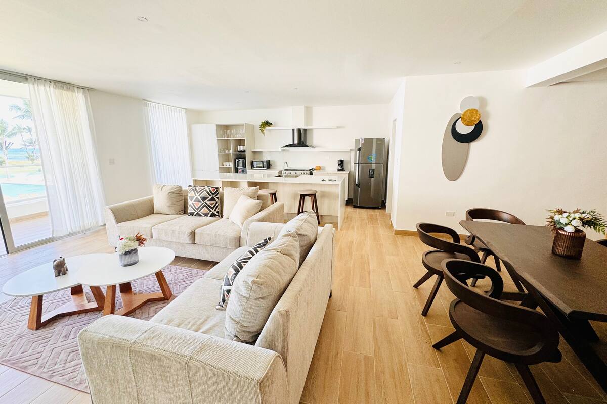 Un salon moderne comprenant un canapé, une table à manger avec des chaises, un coin cuisine avec un réfrigérateur et une grande fenêtre avec des rideaux.