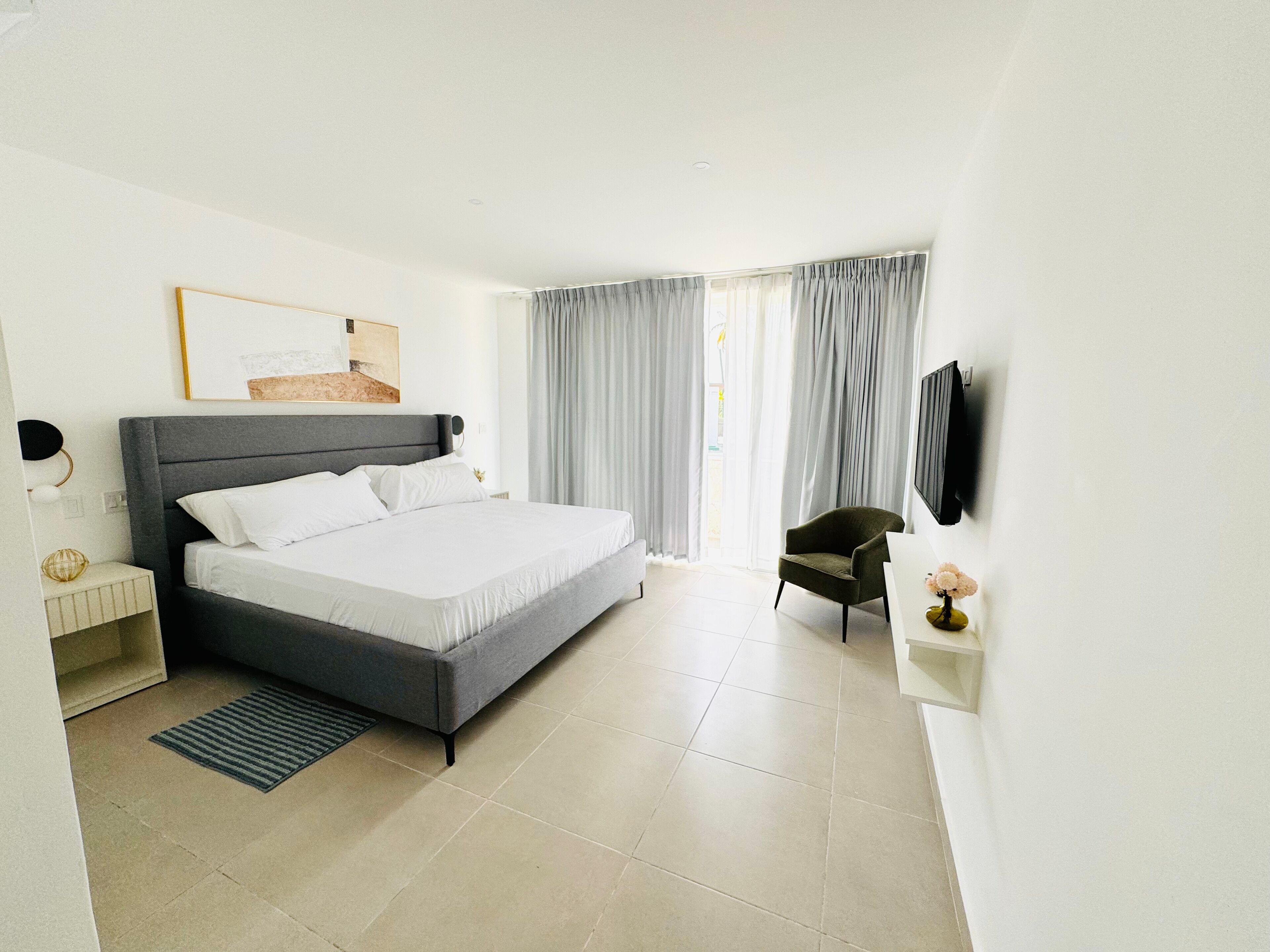 A modern hotel room with a large bed, a chair, a TV, and a window with curtains.