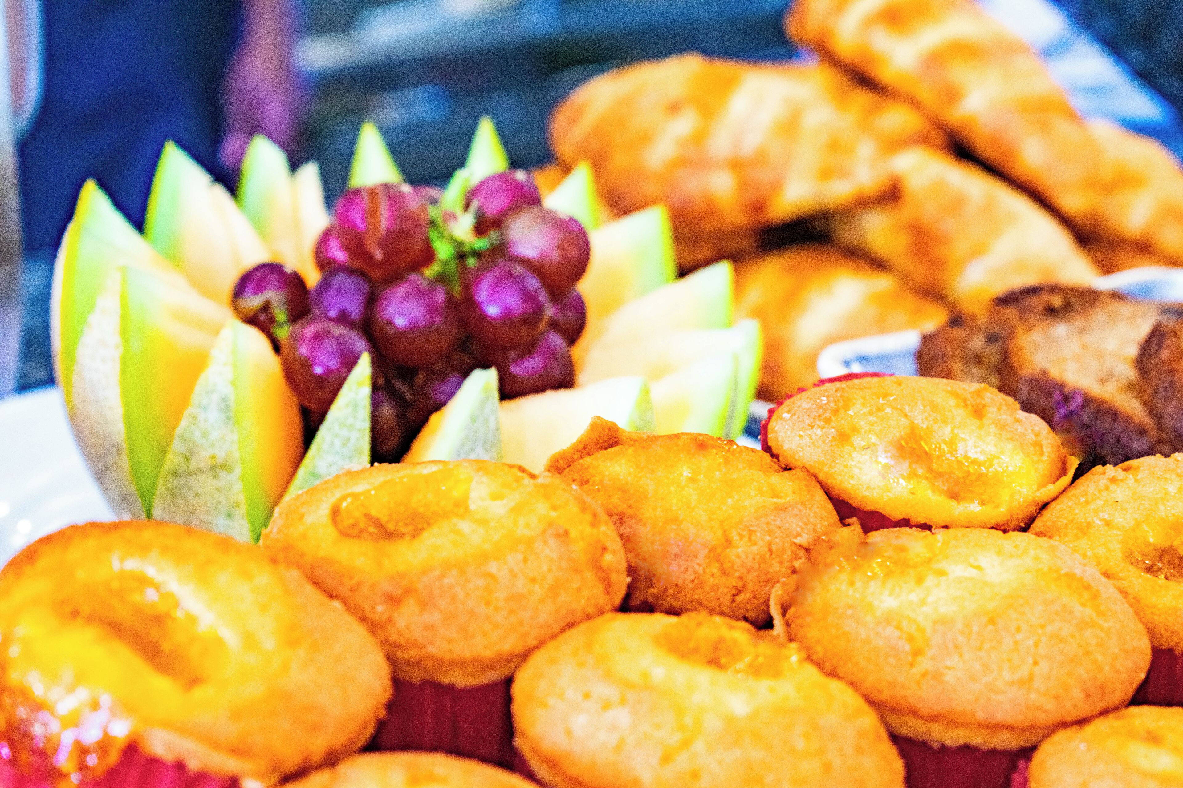 Une variété de produits de boulangerie, notamment des muffins et des pâtisseries, présentés sur une assiette avec des fruits frais, comme des raisins et des tranches de melon.