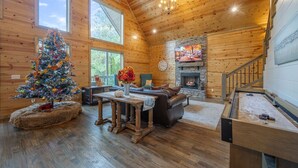 A cozy cabin interior with a wooden interior, a fireplace, a television, and a Christmas tree.