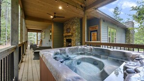 A hot tub on a wooden deck with a stone fireplace and a ceiling fan.